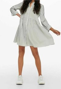 Sukienka zapinana na guziki w jasnym zielonym kolorze z białymi pionowymi paskami. Posiada luźny krój, rękawy o długości 3/4 oraz rozkloszowany dół. Zestawiona z trampkami.