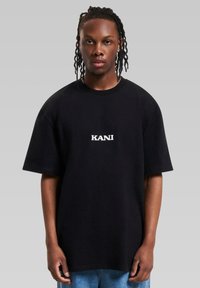 Black oversized cotton t-shirt featuring a white embroidered "KANI" logo at the center, with short sleeves and a round neckline.