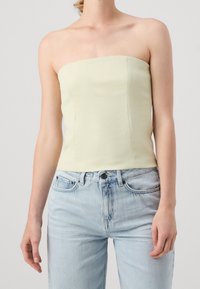Top sans bretelles en vert pastel clair avec un design ajusté. Texture lisse et lignes épurées, associé à un jean en denim bleu clair à taille haute.