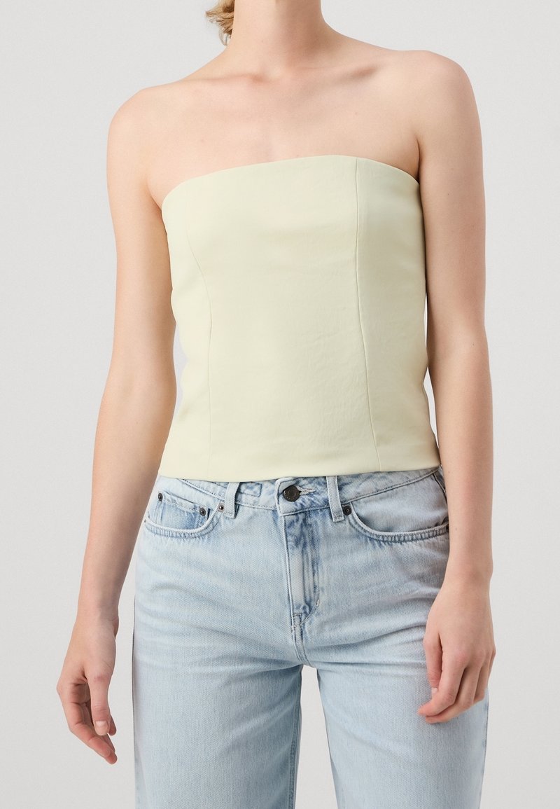 Top sans bretelles en vert pastel clair avec un design ajusté. Texture lisse et lignes épurées, associé à un jean en denim bleu clair à taille haute.