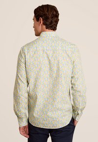 Lichtgele overhemd met knopen, bedekt met een bloemenpatroon met blauwe en groene bladeren. Lange mouwen en een gebogen zoom. De stof lijkt licht van gewicht.