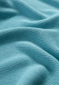 Tissu texturé bleu clair avec un motif en côtes, montrant un tricot doux et un léger éclat ; drapé en plis délicats mettant en valeur sa flexibilité.