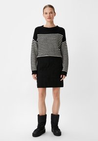 Gestreifter Strickpullover in Schwarz-Weiß mit rundem Ausschnitt, kombiniert mit einem strukturierten schwarzen Rock und schwarzen, mit Fell gefütterten Winterstiefeln.