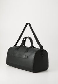 Black duffel bag crafted from smooth synthetic material, featuring dual handles, an adjustable strap, and a sleek rounded design with minimal accents.