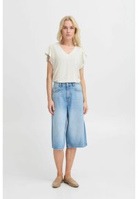 Light beige V-neck top with ruffle sleeves, paired with mid-rise, loose-fitting light blue denim culottes and beige slip-on shoes.