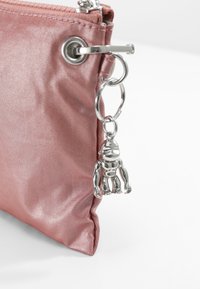 Rosa metallisk tygpåse med en silverfärgad nyckelring som har en liten figurcharm fäst vid en dragkedja. Texturerad yta med glans.
