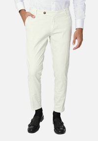 Chinos bianchi in cotone, slim fit, design a cinque tasche, con chiusura a bottone e una leggera texture. Indossati con mocassini in pelle nera e calze.