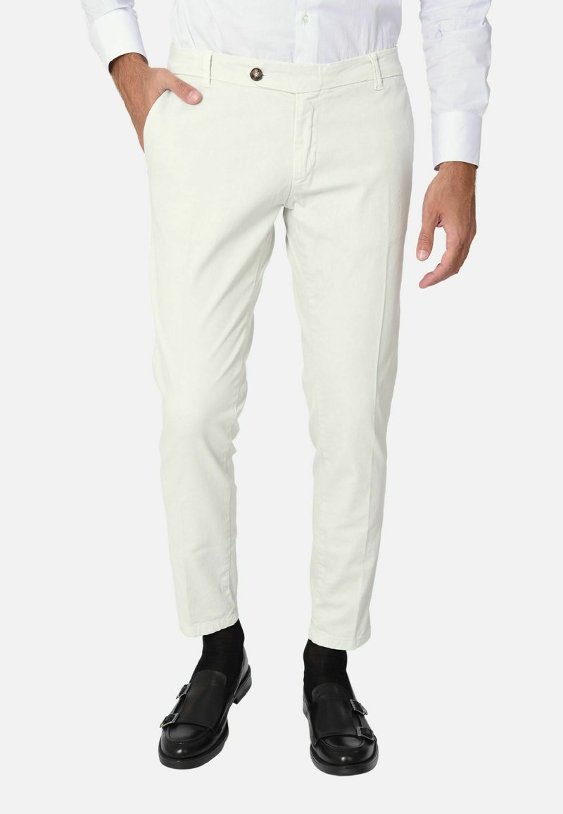 Chinos bianchi in cotone, slim fit, design a cinque tasche, con chiusura a bottone e una leggera texture. Indossati con mocassini in pelle nera e calze.