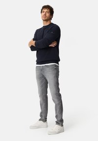Navy sweatshirt with knit texture; gray jeans with a slim fit; white sneakers. Displaying arms crossed, standing against a plain background.
