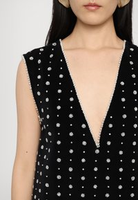 Μαύρο βελούδινο φόρεμα χωρίς μανίκια με βαθύ V-ντεκολτέ, διακοσμημένο με κρυστάλλινες ανθισμένες λεπτομέρειες και κεντημένη περιφέρεια γύρω από το ντεκολτέ.