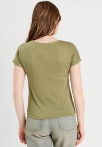 T-shirt vert à manches courtes avec un col rond et des manches retroussées. Le tissu semble doux avec une texture subtile.