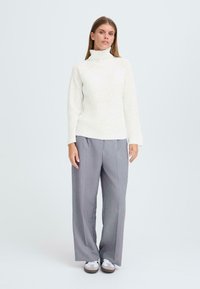 Vit ribbad polotröja med långa ärmar, tillsammans med ljusgrå vida byxor och vita sneakers. Enkelt, rent design.