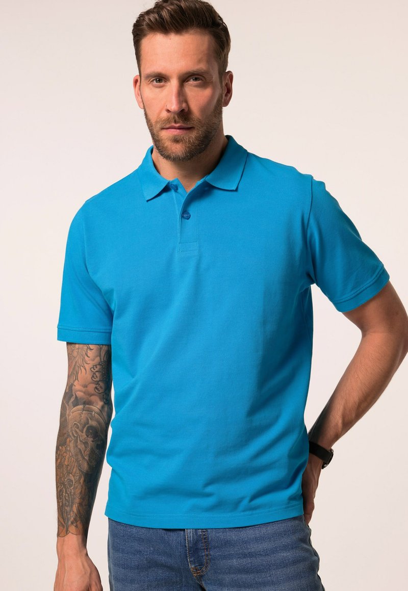 Turquoise polo shirt gemaakt van gladde stof, met een kraag, korte mouwen en een knoopsluiting. Weergegeven met een getatoeëerde arm.