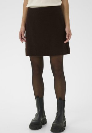 Jupe A-line marron en tissu doux, avec une texture lisse et une coupe mi-genoux. Assortie à des bottines noires et des collants transparents.