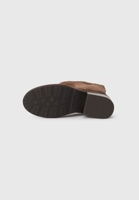 Botte en suède marron, à bout arrondi, avec un petit talon carré et une semelle extérieure en caoutchouc texturé. Comprend une fermeture éclair sur le côté et un détail logo en relief.