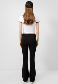 Zwarte flared broek en een cropped wit t-shirt met zwarte afwerkingen. De outfit wordt aangevuld met een zwarte mesh baseballpet.
