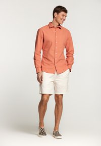 Camisa de manga larga a rayas rojas y blancas, con diseño de botones, combinada con pantalones cortos blancos y zapatillas de lona a rayas en blanco y negro.
