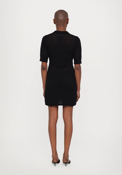 Schwarzes Strickkleid mit kurzen Ärmeln, das über kleine Löcher im Stoff verfügt, eine taillierte Form hat und einen gerippten Kragen besitzt.