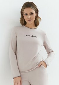 Jasnoróżowa, długorękawowa bluzka z okrągłym dekoltem i czarnym haftowanym napisem "Mom Amie" na piersi. Miękki materiał o gładkiej fakturze.