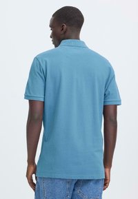 Polo en coton bleu clair avec une coupe décontractée, manches courtes et un col tricoté texturé. Détail de couture notable à l'ourlet.