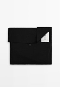 Borsa piegata nera per indumenti con chiusura a bottone e etichetta bianca parzialmente visibile che mostra un'illustrazione di pantaloni e il nome del marchio.