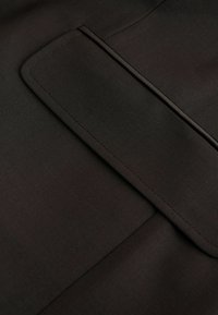 Dunkler Stoff mit glatter Textur und einer flachen Tasche. Das Design ist minimalistisch, ohne sichtbare Muster oder Hardware-Akzente.