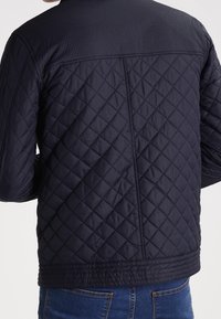 Marinegevoerd jasje met een gestructureerd schouderontwerp en zoom, gekenmerkt door diamantpatronen en minimalistische stiksels.