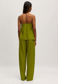 Grüner gestrickter ärmelloser Oberteil, kombiniert mit locker sitzenden grünen Hosen. Schlichte, entspannte Silhouette mit einer glatten Textur.