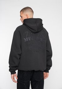 Black hoodie with a textured graphic design on the back, featuring stitched lettering. Fabric appears cotton-blend, has a relaxed fit and hood.