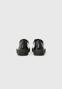Chaussures en cuir verni noir avec une forme arrondie, dotées d'une semelle en caoutchouc noir texturé et d'un simple détail de boucle à l'arrière.