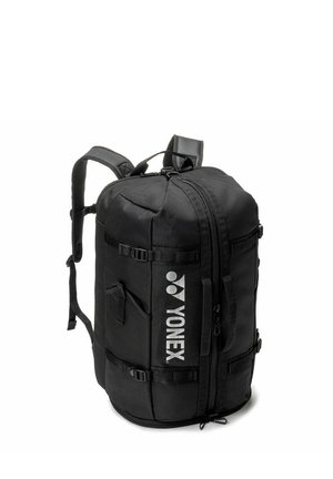 Sac à dos cylindrique noir Yonex avec bretelles rembourrées, poche latérale et logo de la marque vertical, debout sur un fond blanc.
