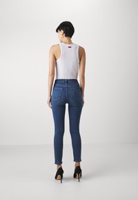 Jean en denim bleu moulant avec une taille haute, dotée de poches arrière et de coutures discrètes. Associé à un débardeur blanc et des talons noirs.