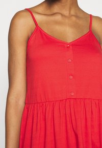 Robe sans manches rouge avec un décolleté en V, devant à boutons et taille froncée ; fabriquée en tissu doux et léger avec une texture lisse.