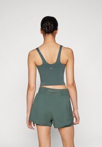 Zelen športni crop top z širokimi naramnicami in majhnim logotipom, v kombinaciji z ohlapnimi kratkimi hlačami, ki imajo elastičen pas.