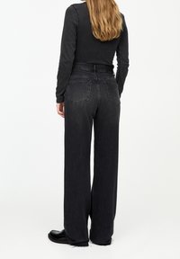 Black wide-leg jeans made of denim with a ripped hem, featuring a high waist and two back pockets. Paired with a fitted top.