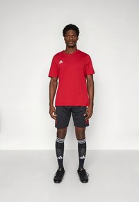 Punane spordisärk, mustad lühikesed püksid ja põlvikuteni ulatuvad mustad sokid valgete triipude ja Adidas logo. Mustad jalgpallijalatsid tekstuursete detailidega.