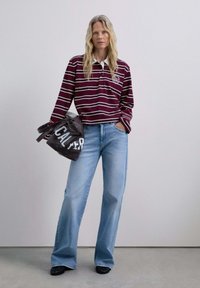 Bordeaux-rot- und weiße gestreifte Langarm-Polo, hellblaue Schlagjeans und eine graue Tragetasche mit "CAL" in Weiß aufgedruckt. Glatte Texturen und lässige Passform.