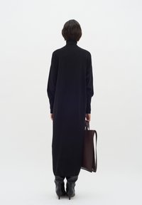 Lång svart tröjdkjol med hög hals, oversized passform och långa ärmar. Kombinationen med knähöga svarta stövlar och en brun läderhandväska.