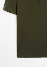 Polo à manches courtes vert olive avec une texture en maille, col et patte de boutonnage, présenté en gros plan sur un fond blanc.