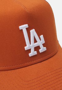 Gorra naranja de tela de algodón con un logo bordado en blanco de "LA" en la parte frontal, con un diseño estructurado y costuras visibles.