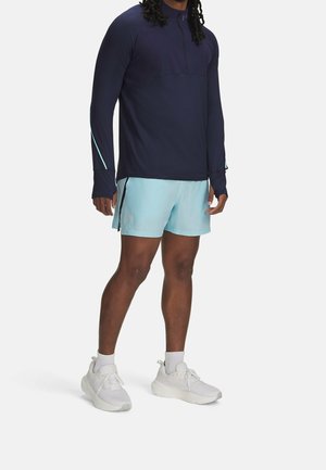 Granatowa sportowa bluzka z długim rękawem i półzamkiem, w połączeniu z jasnoniebieskimi szortami. Białe trampki i dopasowany krój, idealne do aktywności sportowych.