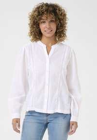 Blusa bianca con bottoni, maniche lunghe a sbuffo, dettagli in pizzo lungo la parte frontale e colletto rotondo, realizzata in un tessuto leggero.
