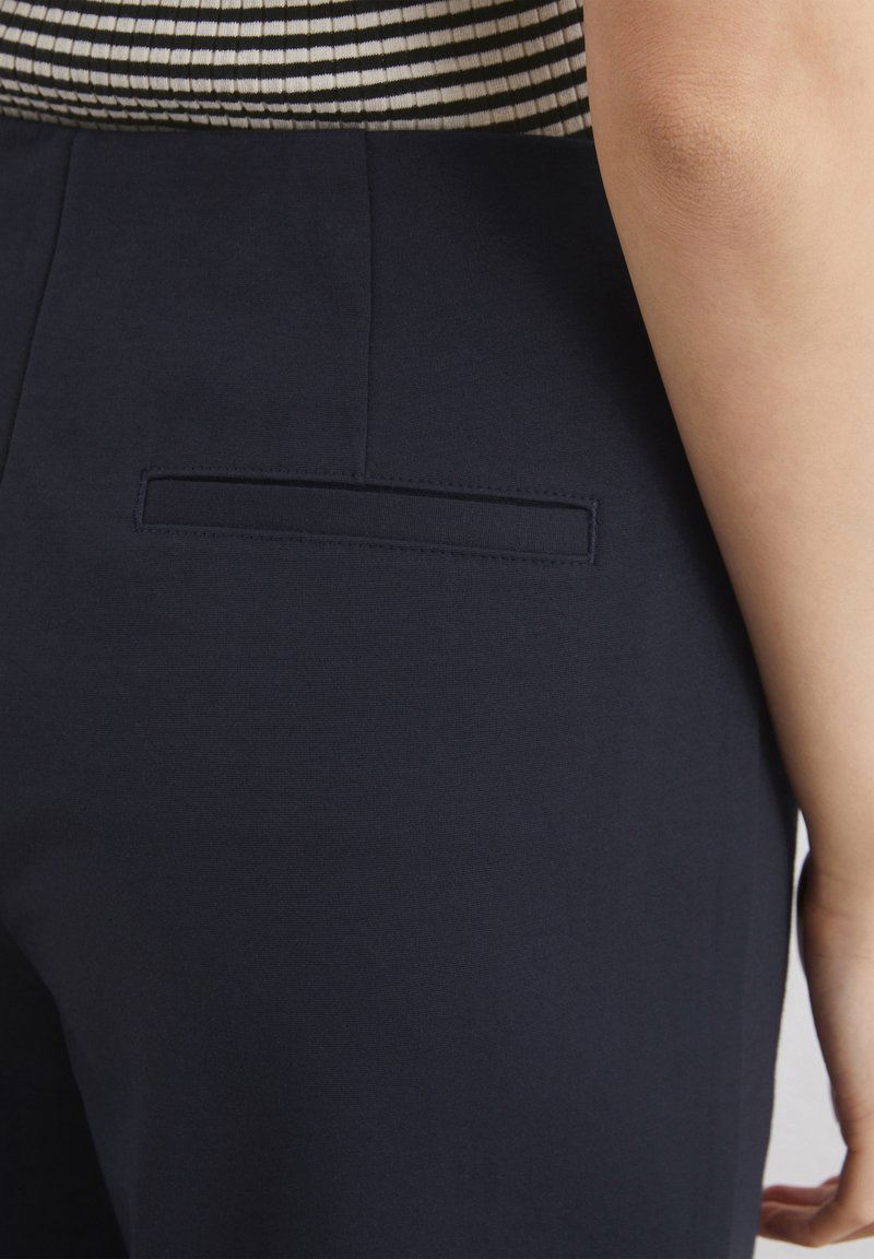 Hosen aus navyblauem Stoff haben eine schlanke Passform, mit einer kleinen, rechteckigen Gesäßtasche und einer glatten Textur. Der Bund ist nicht sichtbar.