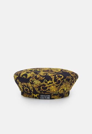Czarna i złota beretka z barokowymi zawijasami, z czarno-białą metką "Versace Jeans Couture" z przodu.