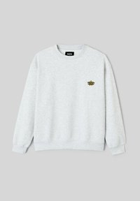 Sweat-shirt gris à col rond en tissu doux, avec poignets et ourlet côtelés. Présente un petit logo brodé en noir et or sur le devant.