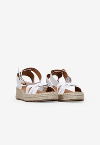Sandalias blancas de espadrille con suelas de yute trenzado, con tirantes cruzados y un hebilla en el tobillo. Textura suave y diseño de punta abierta.
