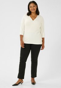 Witte V-hals top met driekwart mouwen, gecombineerd met zwarte getailleerde broek en zwarte slingback schoenen. Gladde stof met een lichte glans.