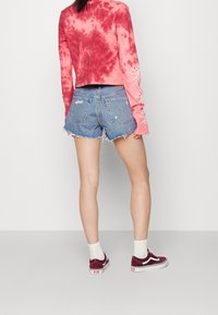 Červený batikovaný crop top s dlouhým rukávem, roztrhané džínové šortky, bílé kotníkové ponožky a bordó boty. Krátký roztřepený lem na šortkách.