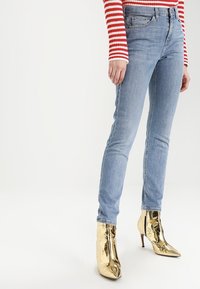 Svetle modré skinny džíny s pěti kapsami, zkombinované s metalickými zlatými kotníkovými botami s špičatou špičkou a jehlovým podpatkem.