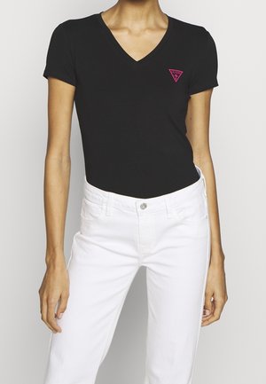 Zwart V-hals T-shirt in slim-fit met klein roze Guess-logo op de borst, gecombineerd met high-waisted witte jeans.
